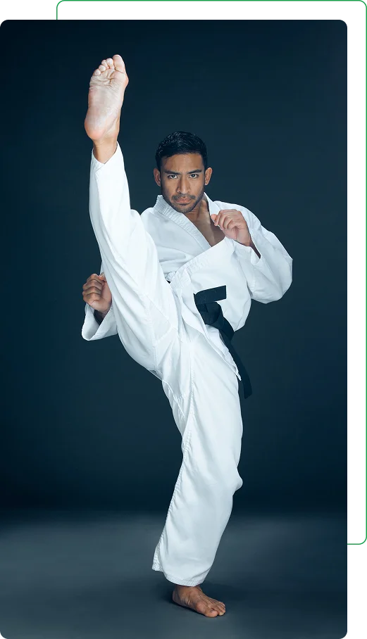 Un homme en gi de karaté blanc et ceinture noire effectue un coup de pied de karaté élevé, dégageant concentration et force, sur un fond gris foncé.